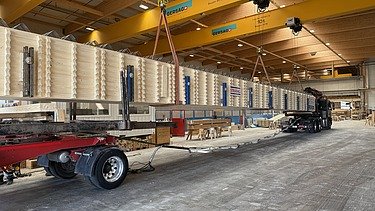 Verladen eines Holzträgers auf einen Lastwagen in einer Halle.