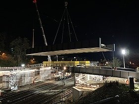Brücke schwebt über der Bahnlinie befestigt an zwei Pneukranen 