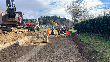  Ein Kran der STRABAG hebt nachts ein langes Brückenteil über Bahngleise. Die Baustelle ist hell erleuchtet.