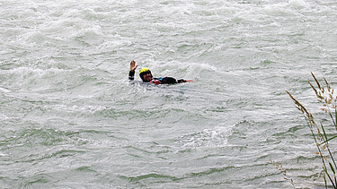 Eine Person in Schutzkleidung treibt während eines Wasserrettungskurses in einem schnell fliessenden Fluss und hebt einen Arm als Signal.