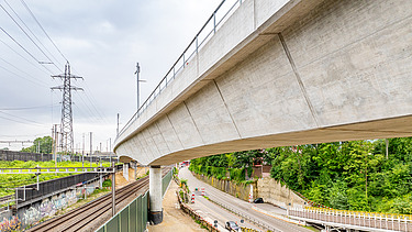  Ein Kran der STRABAG hebt nachts ein langes Brückenteil über Bahngleise. Die Baustelle ist hell erleuchtet.