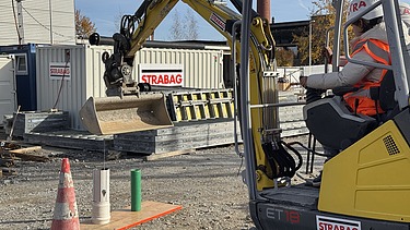 Ein Schüler sitzt im kleinen Bagger und probiert unter Anleitung auf der Baustelle erste Steuerbewegungen aus.