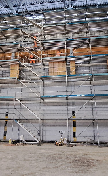 Wand mit Gerüst vom Boden bis zur Decke und eine rote Hebebühne davor