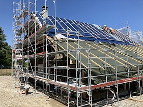 Adlisberghof-Gebäude  in Sanierung, umgeben von Gerüsten und blauer Plane, unter blauem Himmel mit STRABAG Mitarbeiter:innen.
