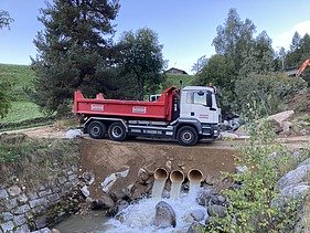 Abtransport - STRABAG Ingenieurbau Ein Lastwagen der STRABAG steht am Aclettbach bei Disentis für den Abtransport bereit. Darunter sieht man Durchlaufrohre mit laufendem Wasser.
