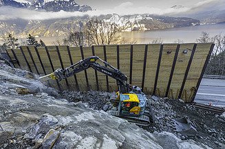 Gelber STRABAG Bagger steht in der Baugrube hinter einer Spundwand und spitzt Felsgestein ab