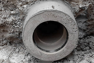 Ein grosses Betonrohr liegt in einer ausgehobenen Erdgrube. Es wird für den Bau einer Kanalisation eingesetzt.