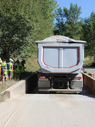 Ein Lastwagen fährt durch ein Wasserbecken damit die Reifen gereinigt werden. Kinder schauen zu.