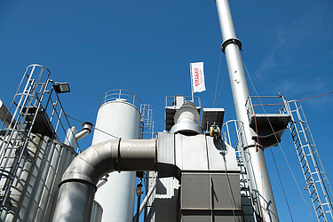 Hohe Metallanlagen und Rohre eines Belagswerks ragen in den blauen Himmel.